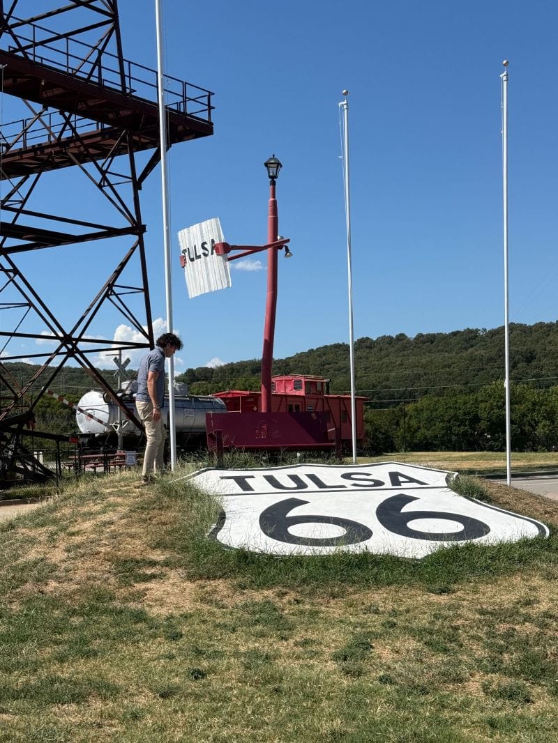 A large Tulsa Route 66 shield painted on the grass beside a railway caboose